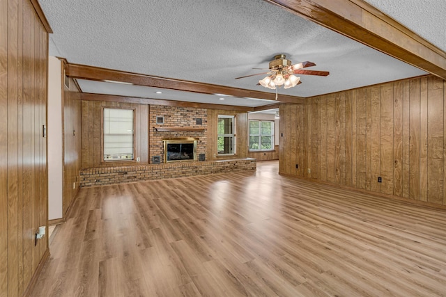 unfurnished living room featuring beam ceiling, ceiling fan, a textured ceiling, light hardwood / wood-style floors, and wooden walls