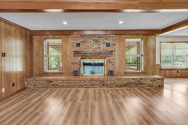 unfurnished living room with a fireplace, beam ceiling, a textured ceiling, light hardwood / wood-style floors, and wood walls