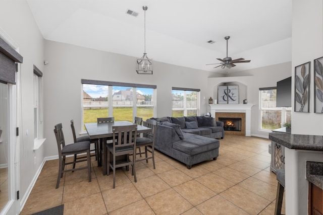 tiled dining area featuring vaulted ceiling, a tile fireplace, a wealth of natural light, and ceiling fan with notable chandelier