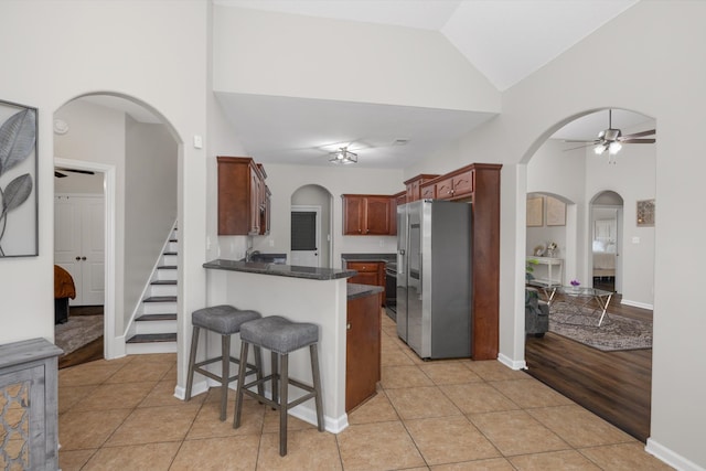 kitchen featuring ceiling fan, high vaulted ceiling, stainless steel refrigerator with ice dispenser, kitchen peninsula, and light wood-type flooring