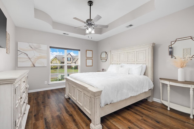 bedroom with dark hardwood / wood-style flooring, a raised ceiling, and ceiling fan