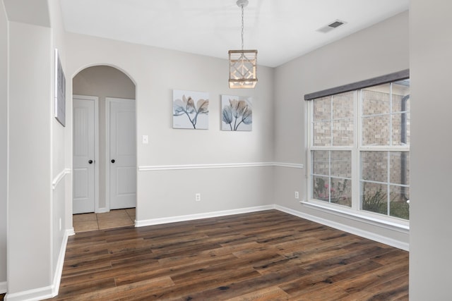 spare room with a chandelier and dark wood-type flooring