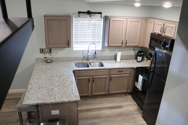 kitchen with light wood-type flooring, light stone countertops, sink, and black appliances