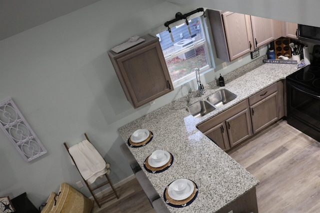 kitchen featuring black range with electric cooktop, sink, light hardwood / wood-style flooring, and light stone counters