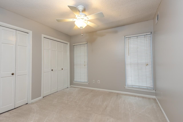 unfurnished bedroom with ceiling fan, light colored carpet, a textured ceiling, and multiple closets