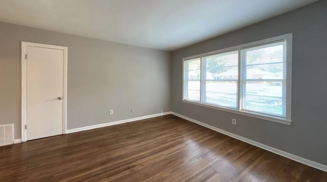 unfurnished room with dark wood-style flooring, visible vents, and baseboards