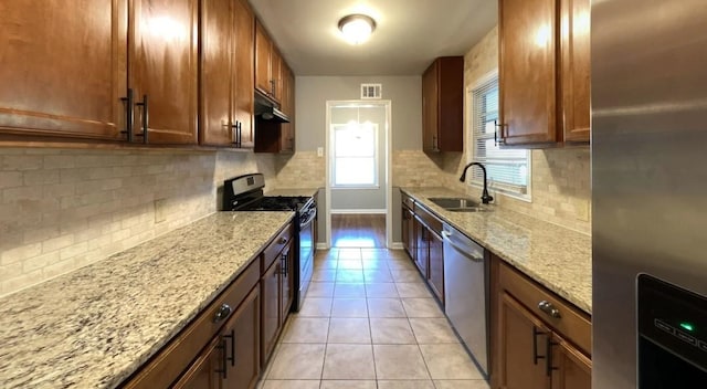 kitchen featuring light tile patterned floors, light stone counters, stainless steel appliances, under cabinet range hood, and a sink