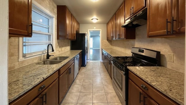 kitchen featuring light stone counters, brown cabinets, stainless steel appliances, a sink, and under cabinet range hood