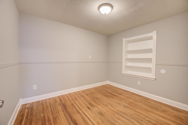 unfurnished room featuring baseboards, wood finished floors, and built in features