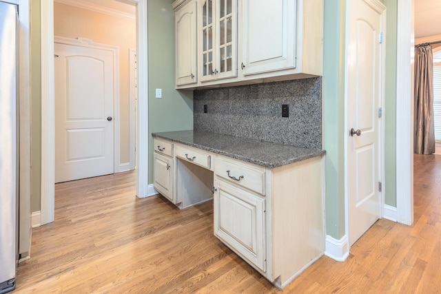 kitchen with tasteful backsplash, ornamental molding, light wood-type flooring, built in desk, and dark stone countertops