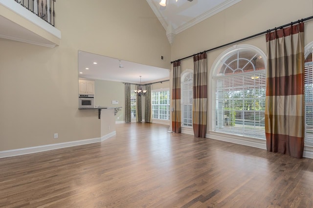 unfurnished living room with hardwood / wood-style flooring, a towering ceiling, an inviting chandelier, and ornamental molding