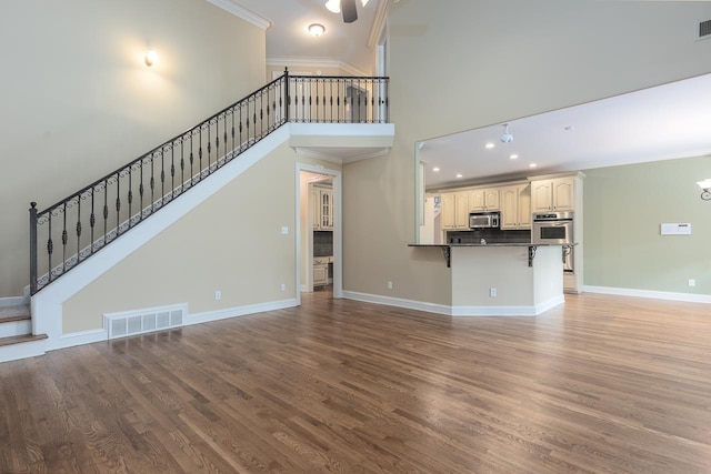 unfurnished living room featuring a high ceiling, hardwood / wood-style floors, and crown molding