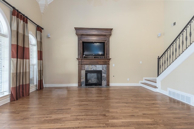 unfurnished living room featuring hardwood / wood-style floors, a tiled fireplace, and a high ceiling