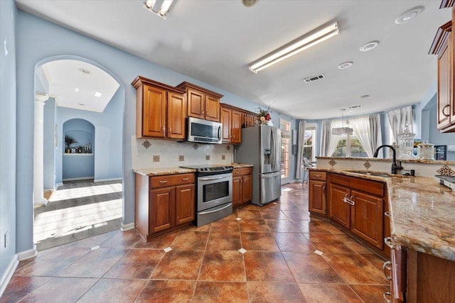 kitchen featuring sink, appliances with stainless steel finishes, light stone countertops, backsplash, and hanging light fixtures