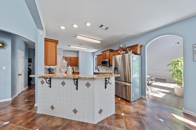 kitchen with kitchen peninsula, light stone countertops, a kitchen bar, and appliances with stainless steel finishes