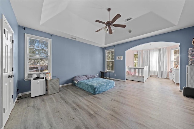 bedroom with multiple windows, a raised ceiling, ceiling fan, and light hardwood / wood-style flooring