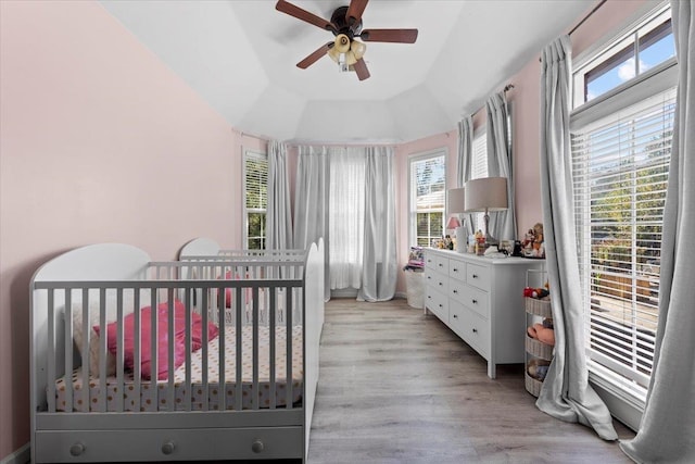 bedroom featuring light wood-type flooring, a nursery area, lofted ceiling, and ceiling fan