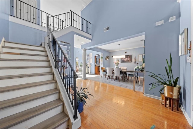 stairway featuring ornamental molding, a towering ceiling, hardwood / wood-style flooring, and decorative columns