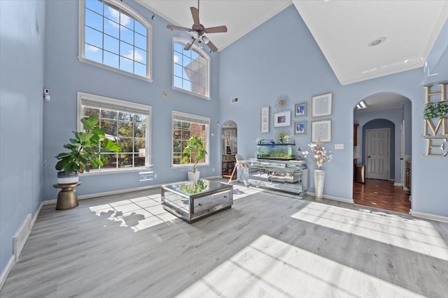 living room with ornamental molding, light wood-type flooring, ceiling fan, and high vaulted ceiling