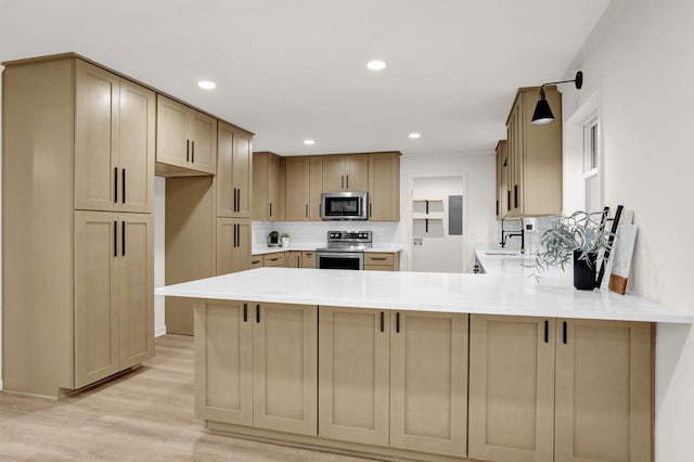 kitchen with stainless steel appliances, sink, decorative backsplash, kitchen peninsula, and light hardwood / wood-style flooring