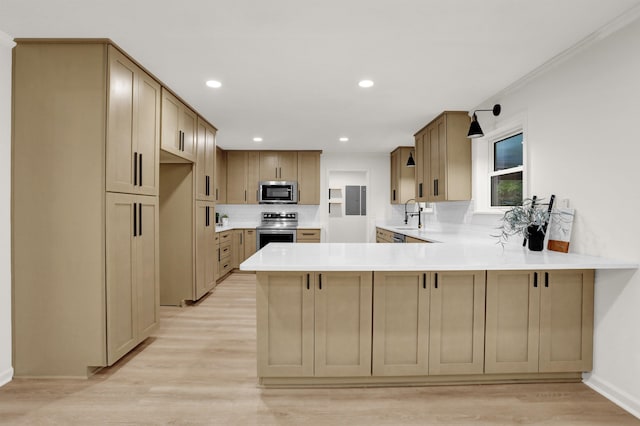 kitchen featuring ornamental molding, kitchen peninsula, appliances with stainless steel finishes, and light wood-type flooring