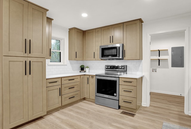 kitchen featuring electric panel, tasteful backsplash, light brown cabinets, light wood-type flooring, and appliances with stainless steel finishes