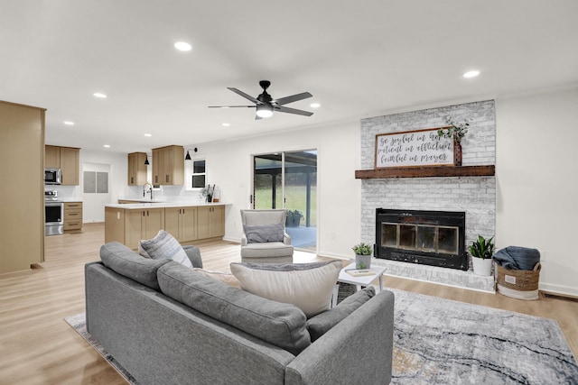 living room featuring light wood-type flooring, sink, ceiling fan, and a brick fireplace