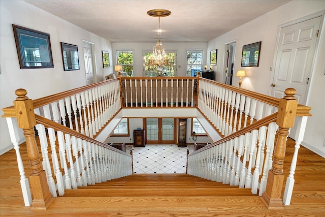 stairs with hardwood / wood-style flooring, a textured ceiling, and a notable chandelier