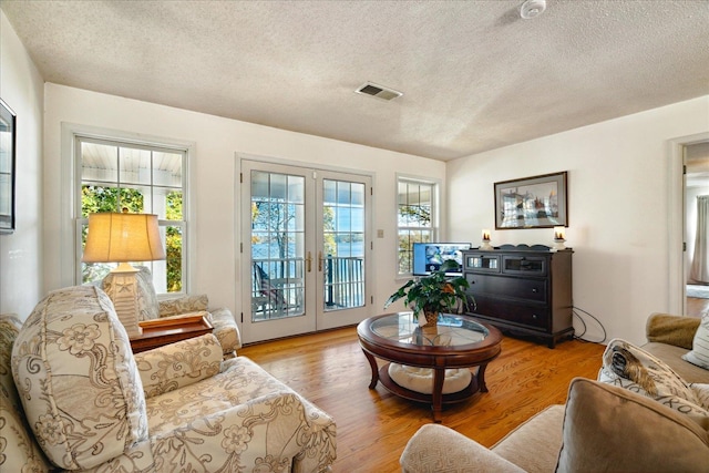 living room featuring a textured ceiling, light hardwood / wood-style flooring, and french doors