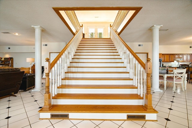 stairs with a textured ceiling, tile patterned floors, and ornate columns