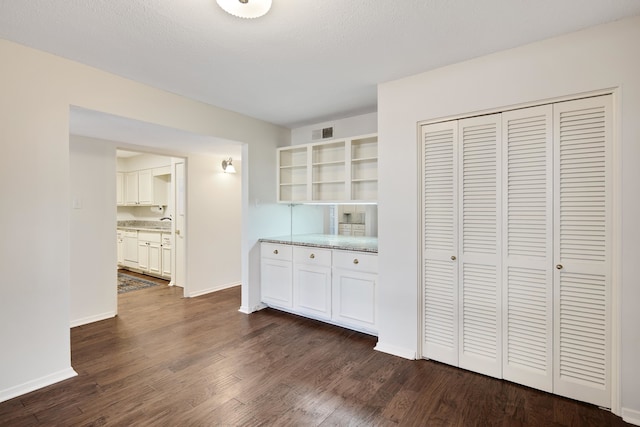 interior space with dark wood-type flooring, white cabinetry, a textured ceiling, and light stone counters