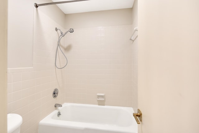 bathroom with toilet, tiled shower / bath combo, and tile walls