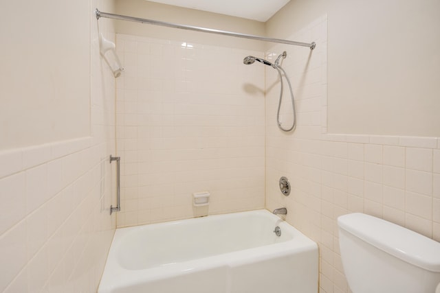 bathroom with tile walls, tiled shower / bath combo, and toilet