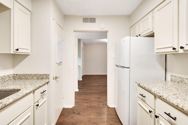 kitchen with dark wood-type flooring, light stone counters, white refrigerator, a textured ceiling, and white cabinetry