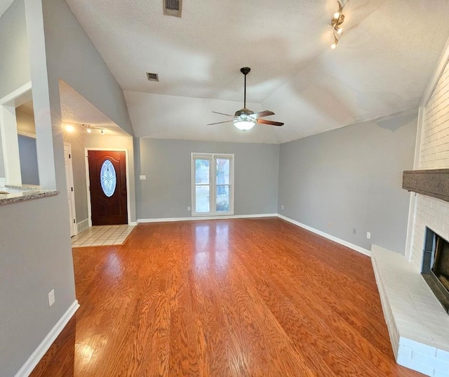 unfurnished living room featuring a fireplace, a textured ceiling, light wood-type flooring, and vaulted ceiling