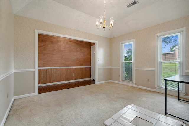 unfurnished room featuring an inviting chandelier, vaulted ceiling, and carpet flooring