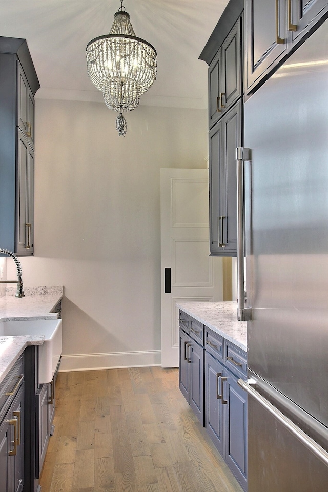 kitchen with crown molding, light wood-type flooring, stainless steel built in fridge, and light stone counters