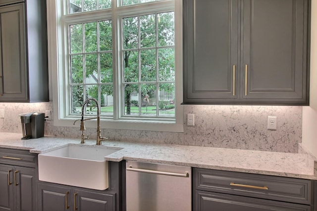 kitchen featuring gray cabinetry, stainless steel dishwasher, sink, and light stone countertops