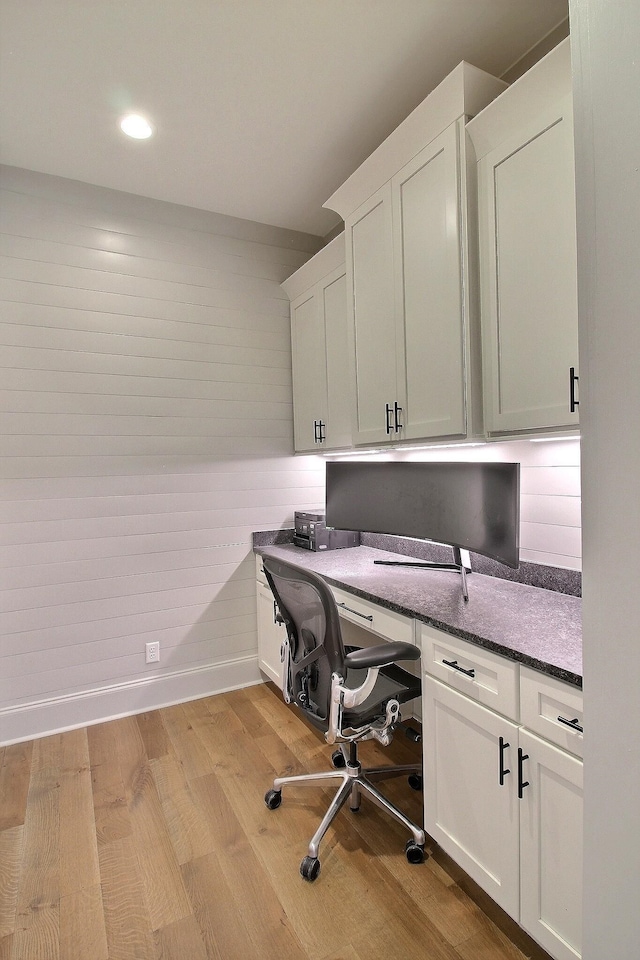 office space with built in desk, wooden walls, and light hardwood / wood-style flooring