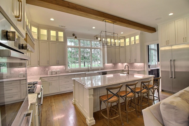 kitchen with light stone counters, stainless steel appliances, backsplash, dark wood-type flooring, and a kitchen island with sink