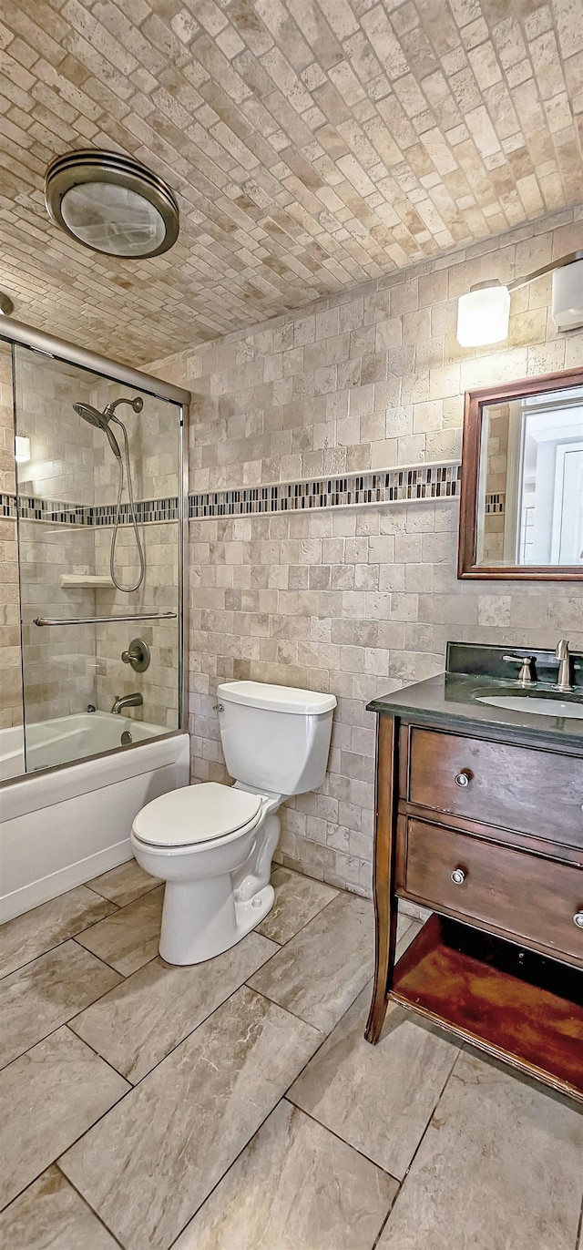 full bathroom featuring tile walls, vanity, combined bath / shower with glass door, and toilet