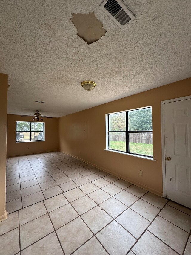 tiled spare room with plenty of natural light, a textured ceiling, and ceiling fan