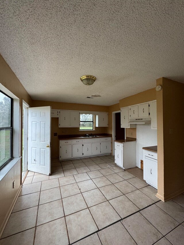 kitchen with sink, a textured ceiling, light tile patterned floors, and white cabinets