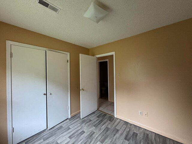 unfurnished bedroom with light hardwood / wood-style flooring, a textured ceiling, and a closet