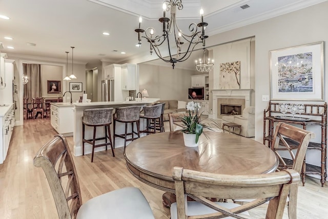 dining room featuring ornamental molding, sink, light hardwood / wood-style floors, a chandelier, and a tile fireplace