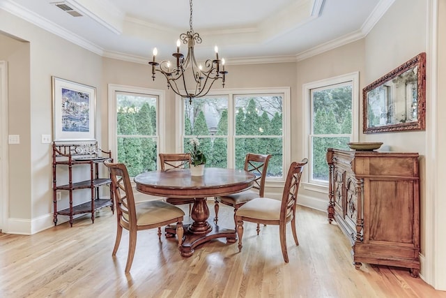 dining area with ornamental molding, light hardwood / wood-style flooring, a tray ceiling, and an inviting chandelier