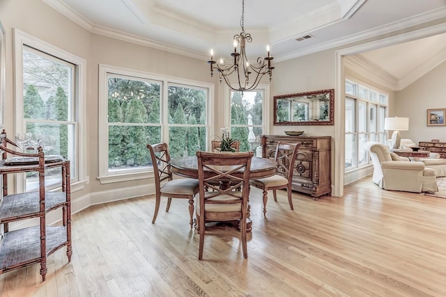 dining space with light hardwood / wood-style floors, a tray ceiling, crown molding, and a notable chandelier