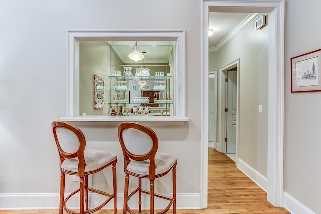 bar featuring hanging light fixtures, light wood-type flooring, and ornamental molding