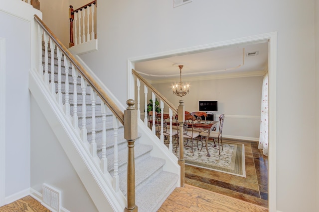 stairway with an inviting chandelier, hardwood / wood-style flooring, and crown molding