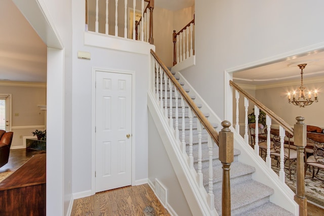 staircase featuring a high ceiling, hardwood / wood-style floors, a notable chandelier, and ornamental molding